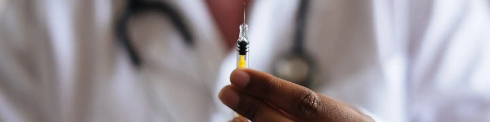 Doctor in a white coat holds up a syringe with a vaccine