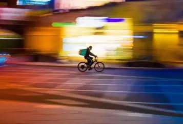 Food delivery worker on bike in London streets at night