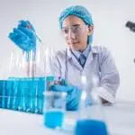 scientist with protective clothing surrounded by medical equipment looking at a test tube
