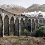 steam train over aqueduct with mountains in background
