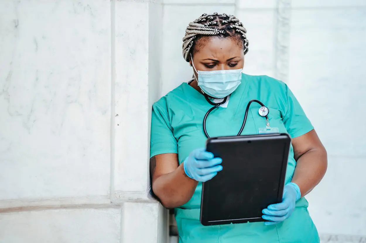 healthcare worker in scrubs and mask holding a tablet computer and looking at it
