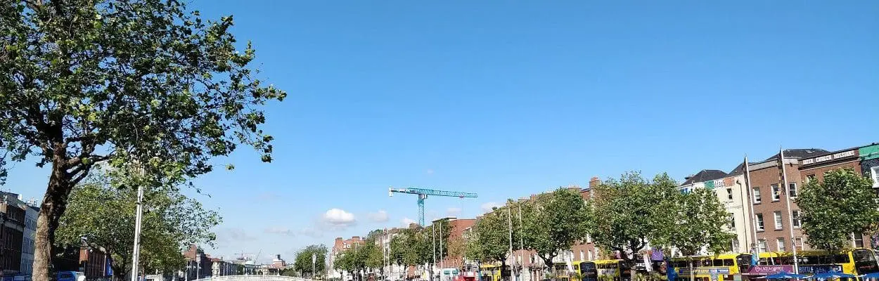 tree lined river with buildings, bridges and walkways against a blue sky