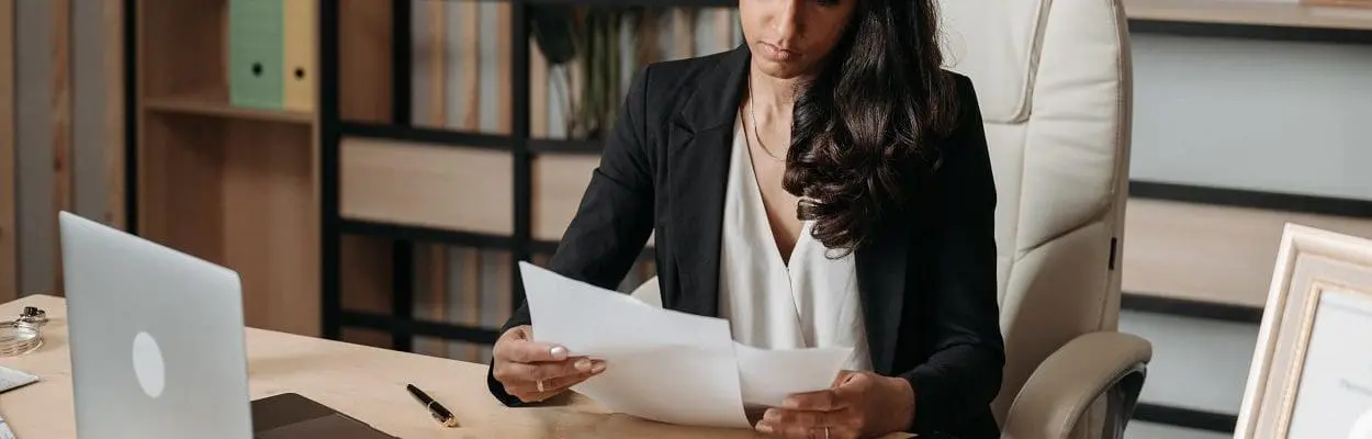 woman in office looking at papers with laptop on desk