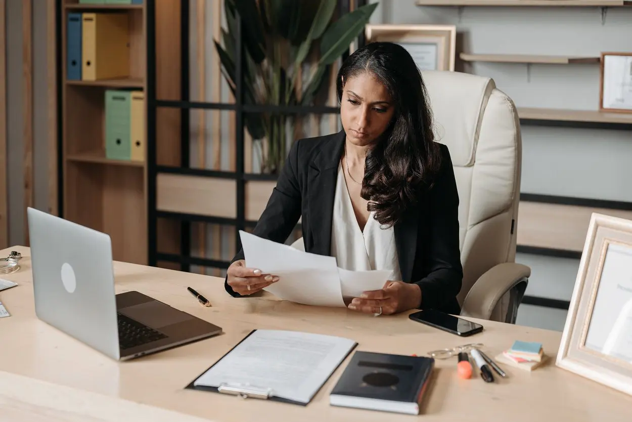 woman in office looking at papers with laptop on desk