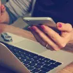 woman holding phone while looking at a laptop