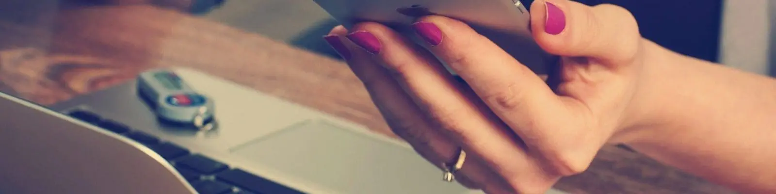 woman holding phone while looking at a laptop