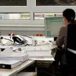 person sitting at desk looking at a computer screen surrounded with paper and files
