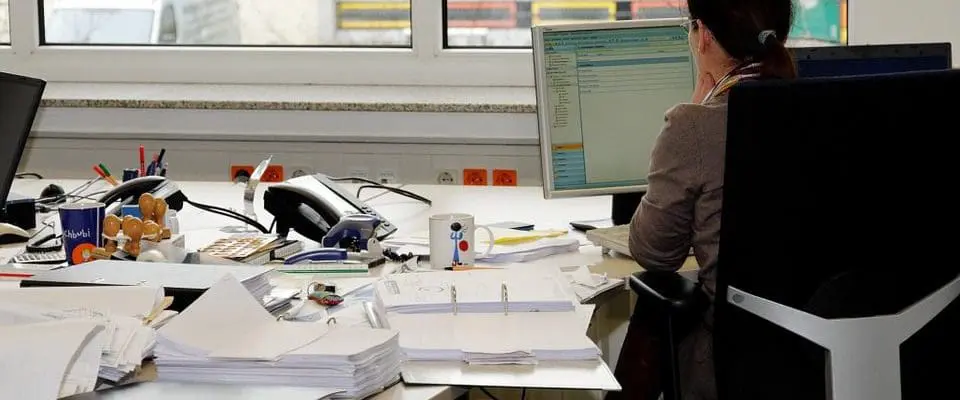 person sitting at desk looking at a computer screen surrounded with paper and files