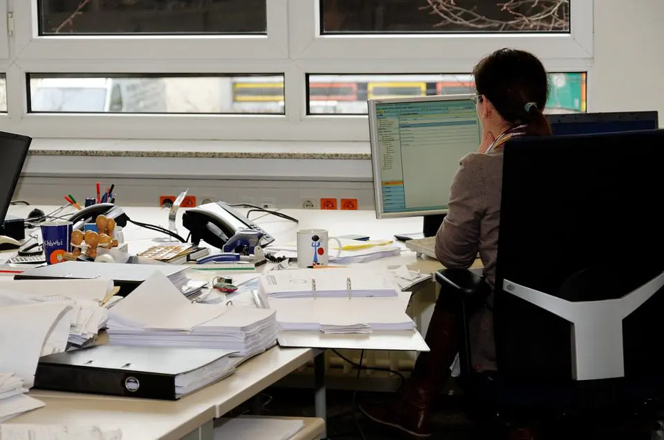 person sitting at desk looking at a computer screen surrounded with paper and files