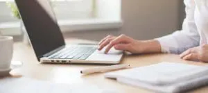 Hand at laptop with notepad and pencil