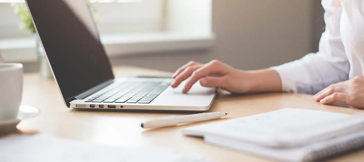 Hand at laptop with notepad and pencil