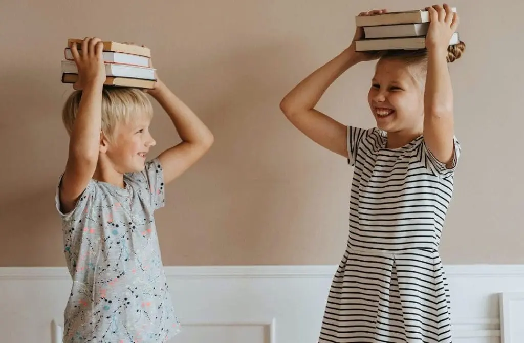 two children holding books on their head and smiling