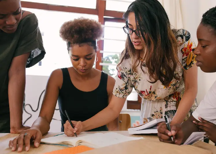People around a table as woman writes on paper