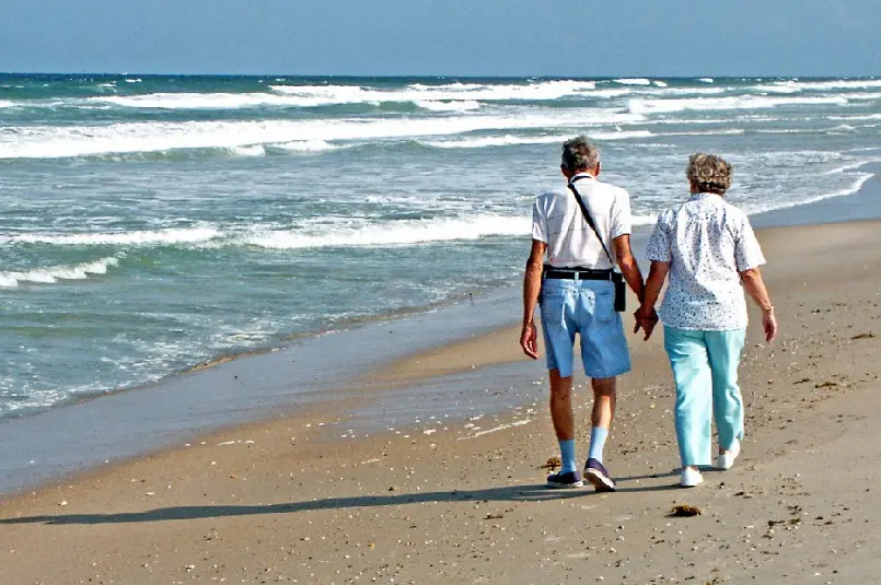 Elderly couple, holding hands and walking at the beach