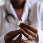 Doctor in a white coat holds up a syringe with a vaccine