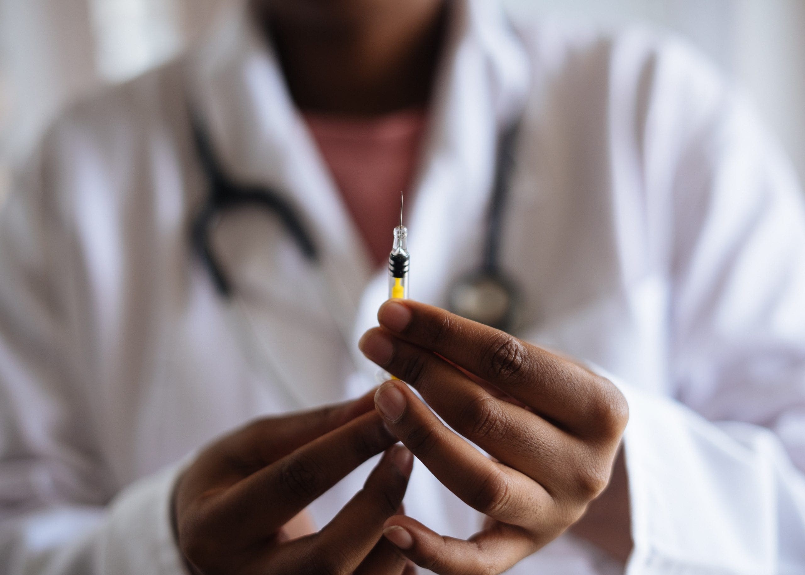 Doctor in a white coat holds up a syringe with a vaccine