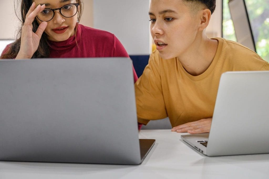 Two people wearing bright clothes looking at a laptop and speaking