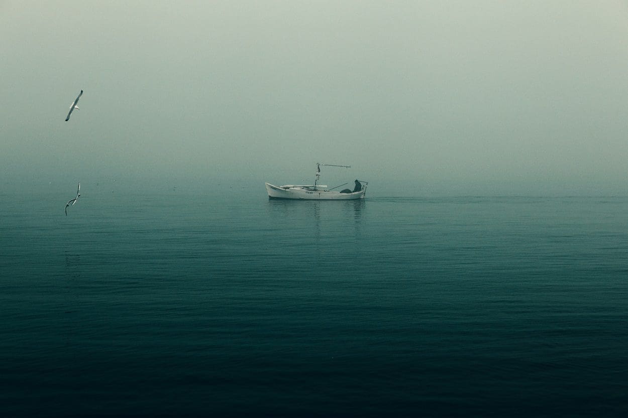 Small board with person on board in sea with a foggy sky