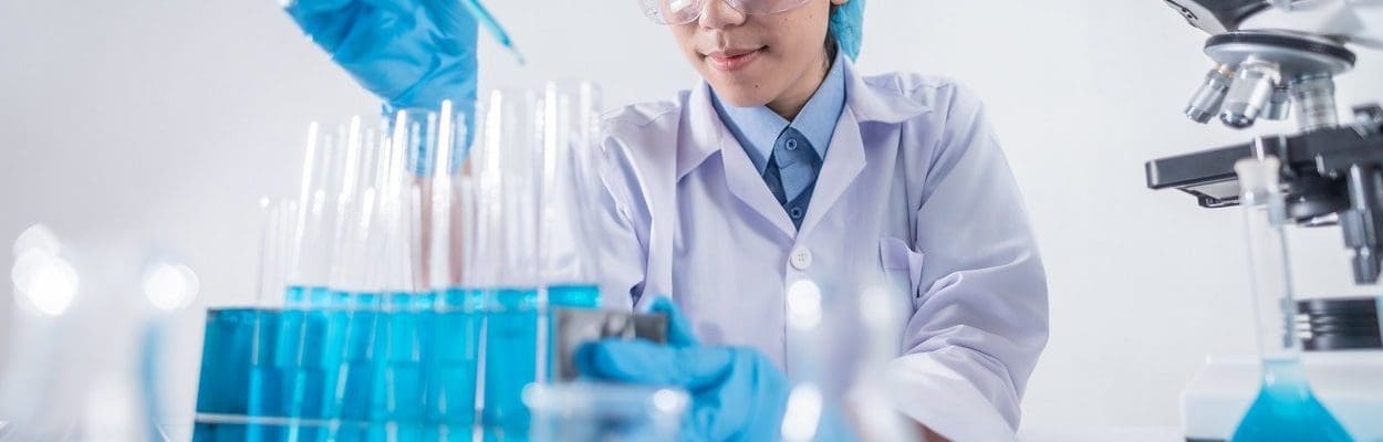 scientist with protective clothing surrounded by medical equipment looking at a test tube