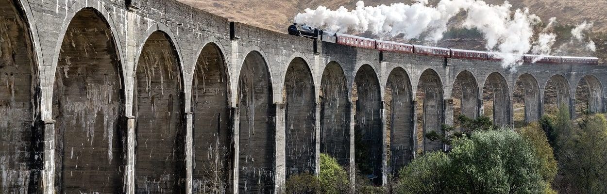 steam train over aqueduct with mountains in background