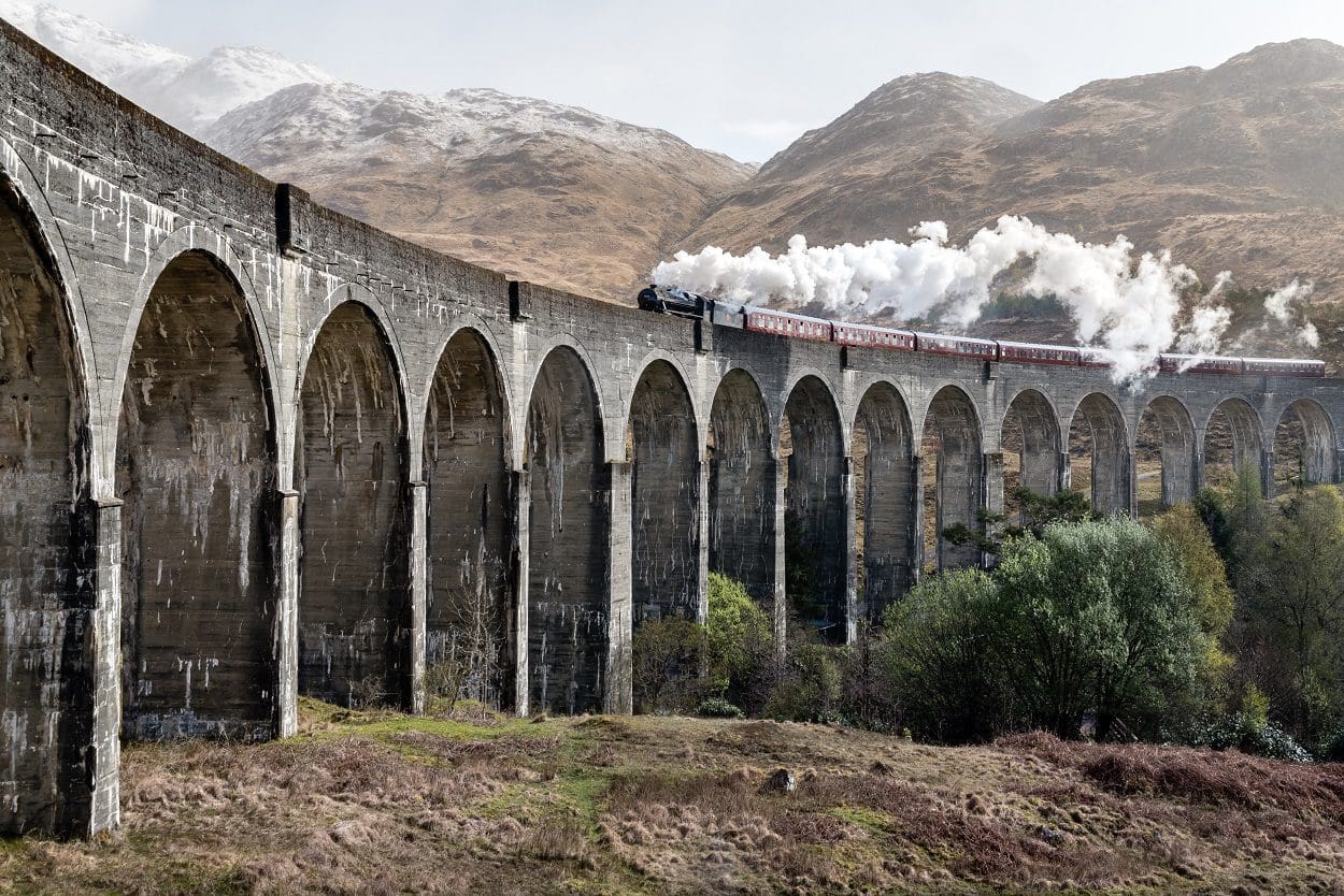 steam train over aqueduct with mountains in background
