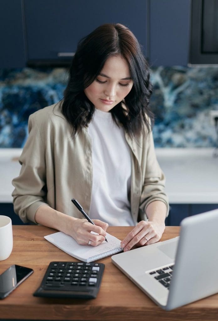 woman writing on a notepad in front of a laptop