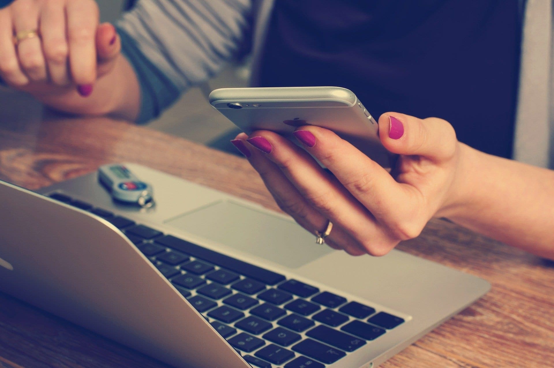 woman holding phone while looking at a laptop