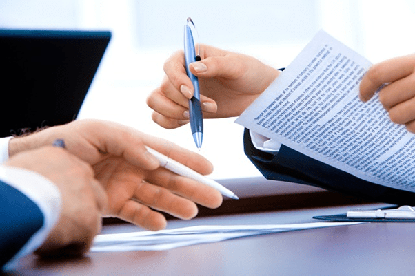 Close up of hands of two people holding pens and looking at formal documents