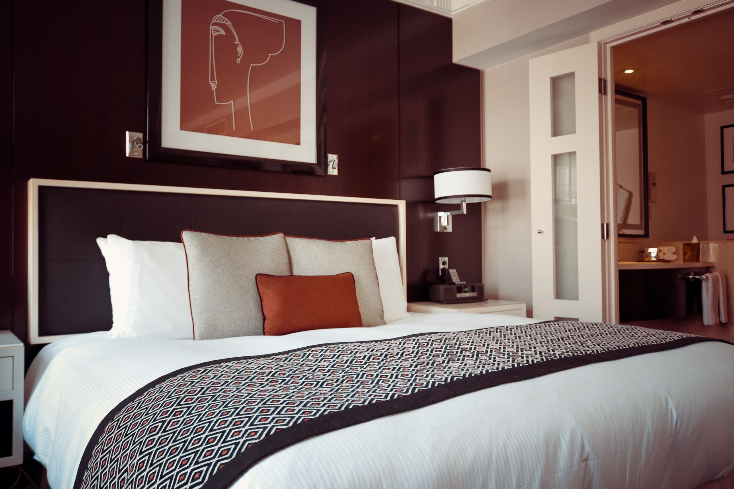 A hotel room with a made bed and a purple feature wall