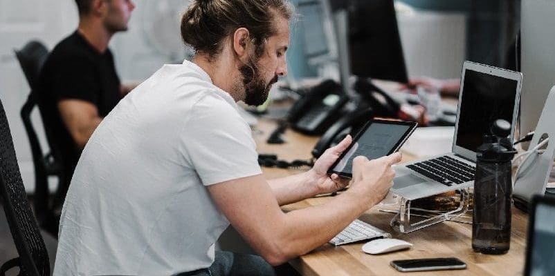Man holding tablet, sitting down in front of computer