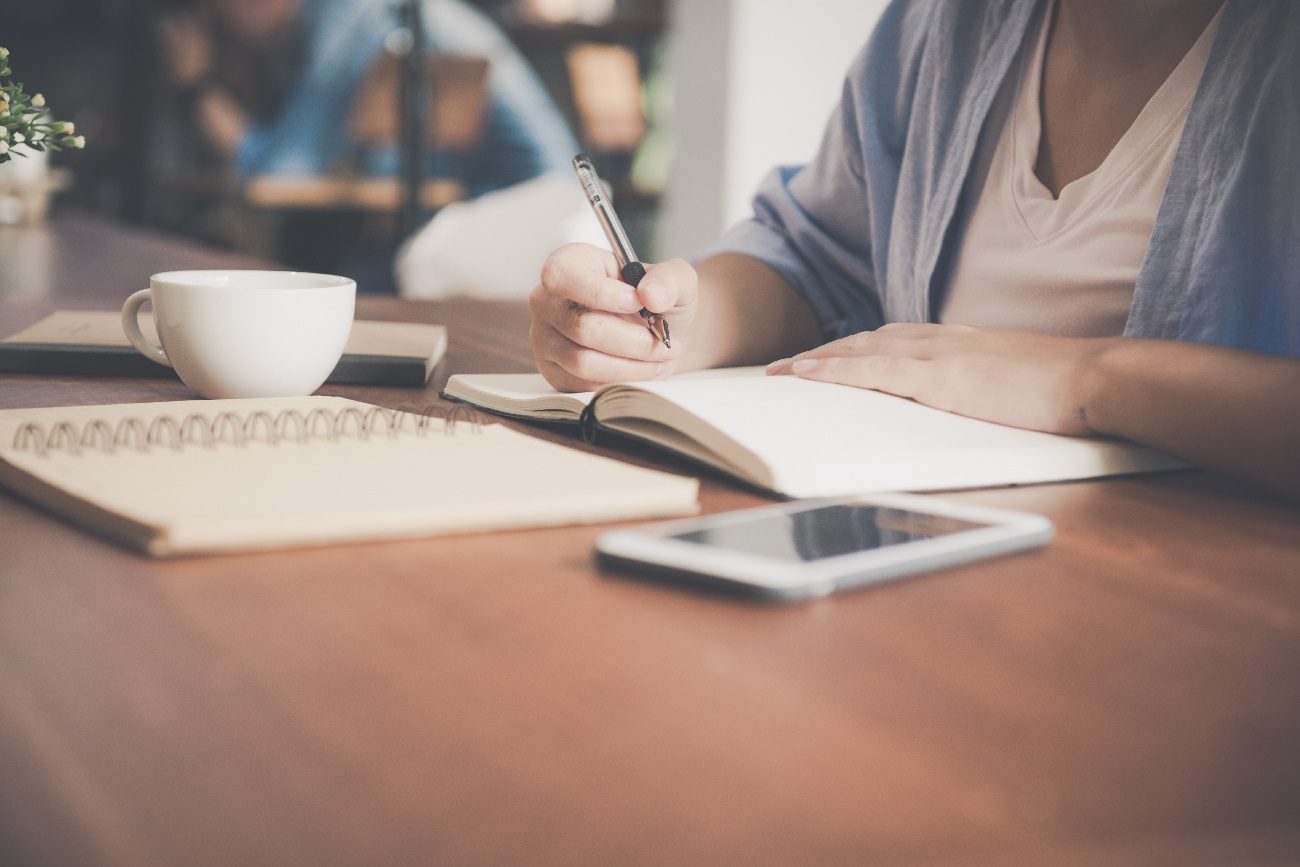 woman writing in a notebook to represent an application being filled out.