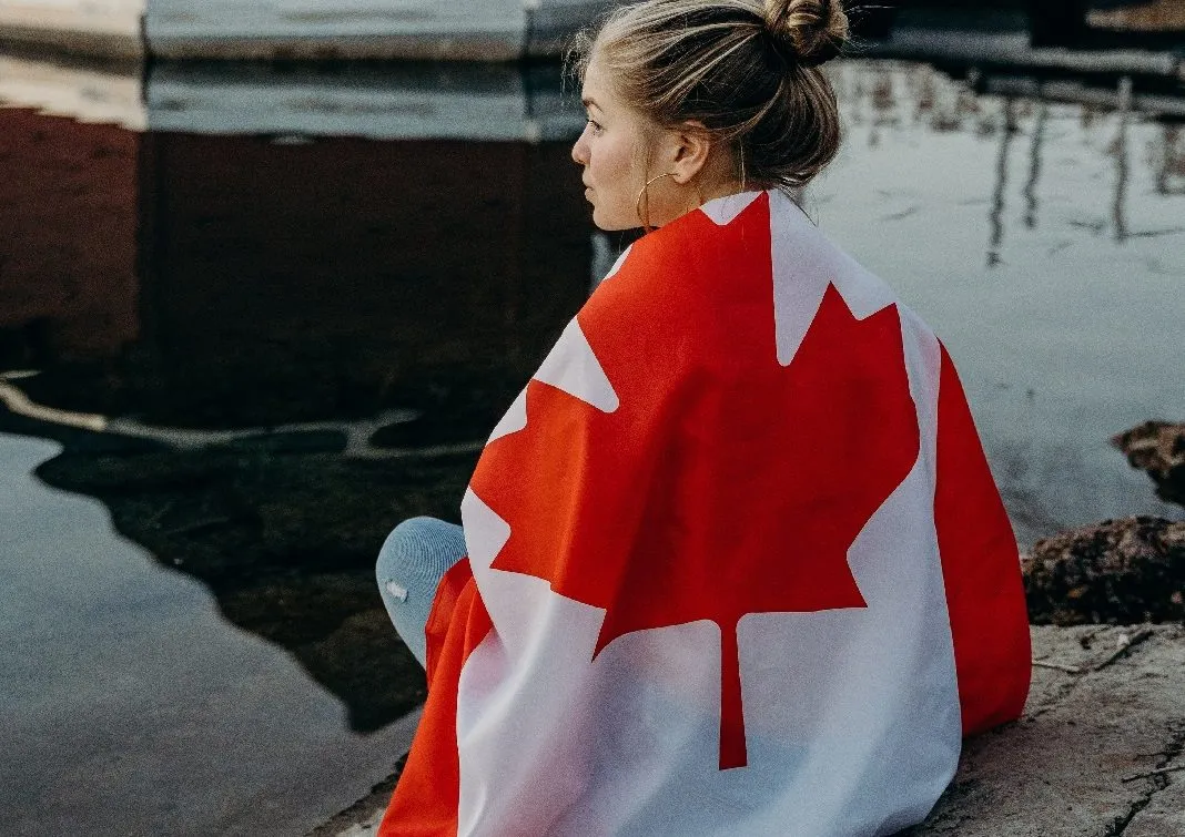 Woman sitting down wrapped in Canadian flag.