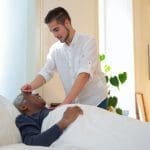 Caregiver checking man's temperature.