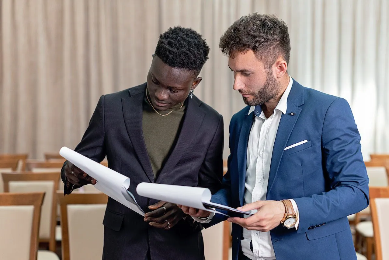 Two men, holding and reading through documents