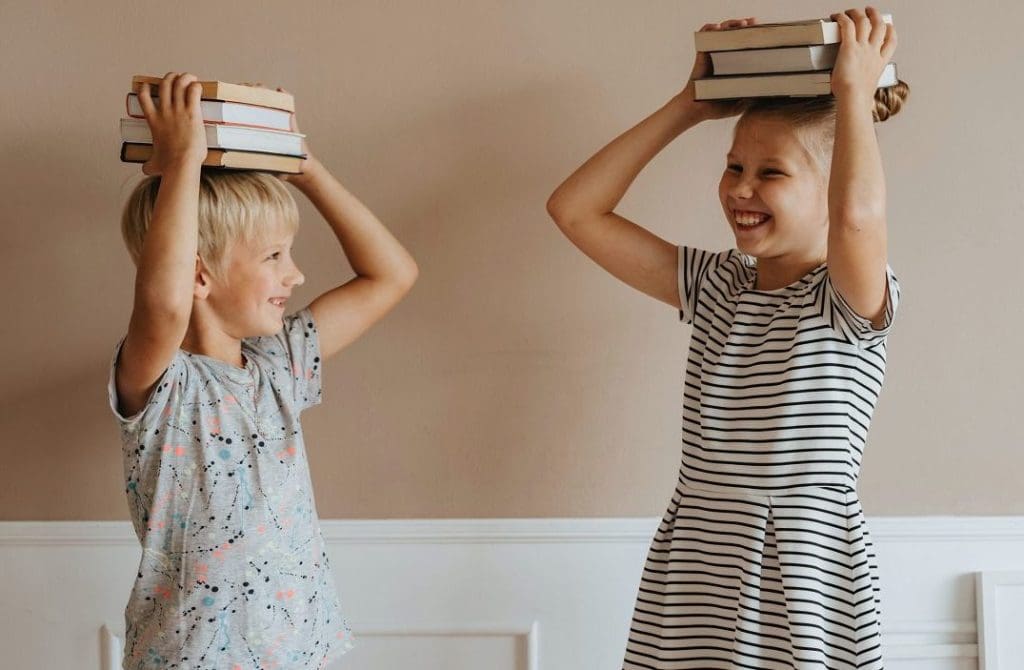 two children holding books on their head and smiling