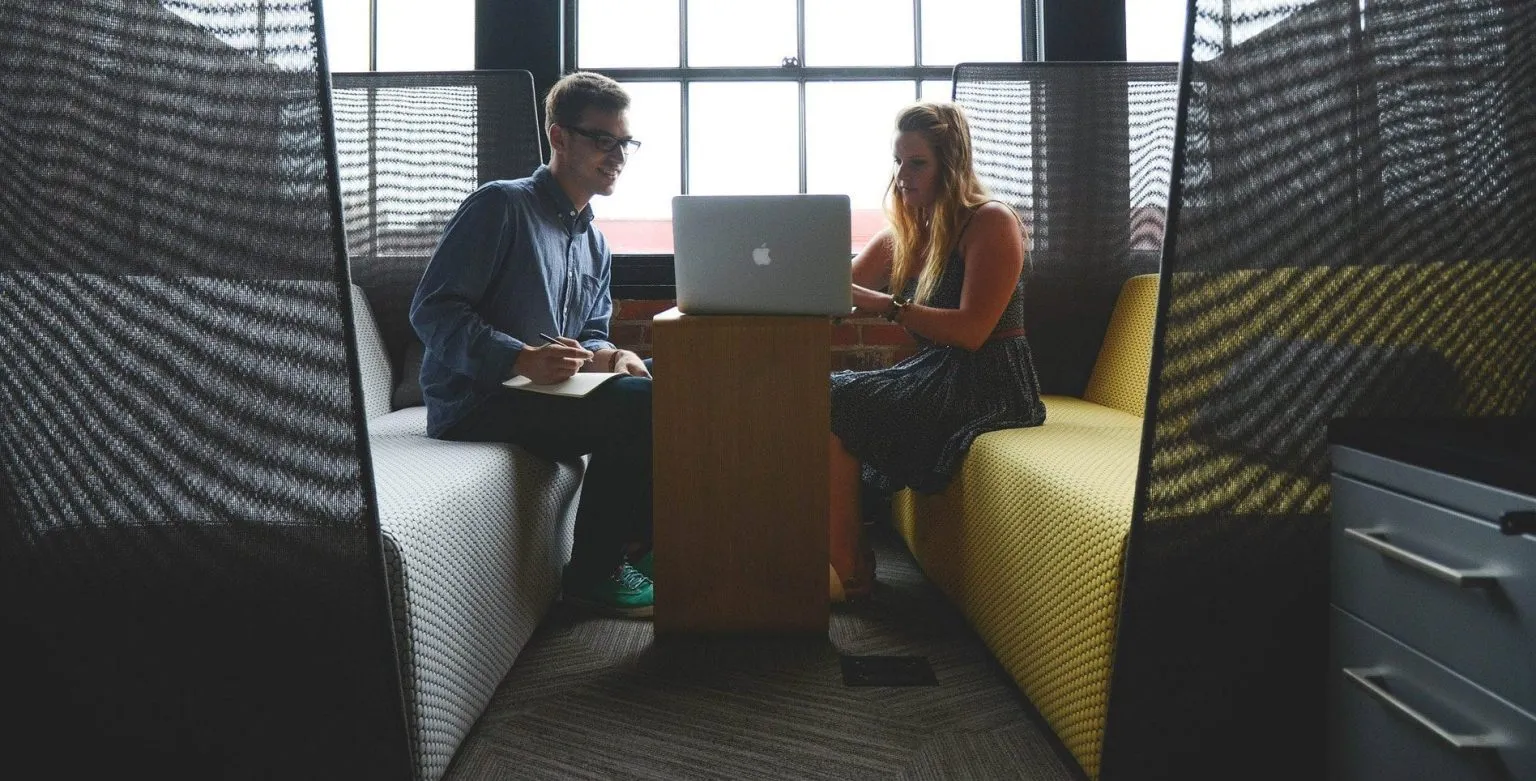 Two office workers sitting in a meeting booth